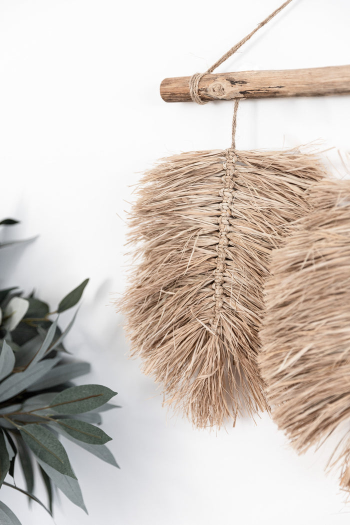 A trio of hand braided raffia leaves hang from a natural driftwood piece found by the coast & completed with a Jute hanger. This wall hanging is ideal for those who love raw texture & the feel of natural materials in their home.